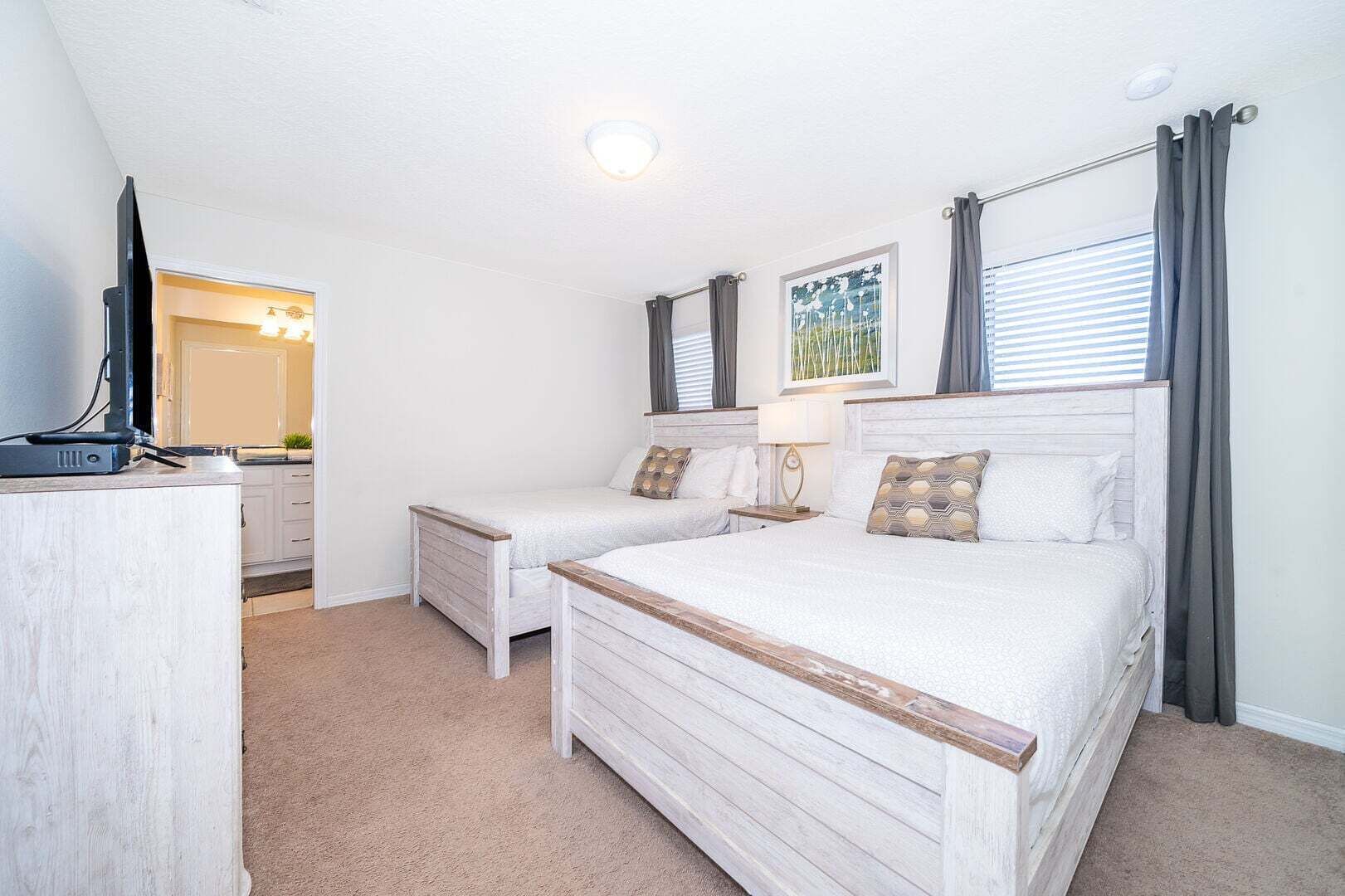 A bedroom with two beds, a desk, a TV, and a window with curtains.