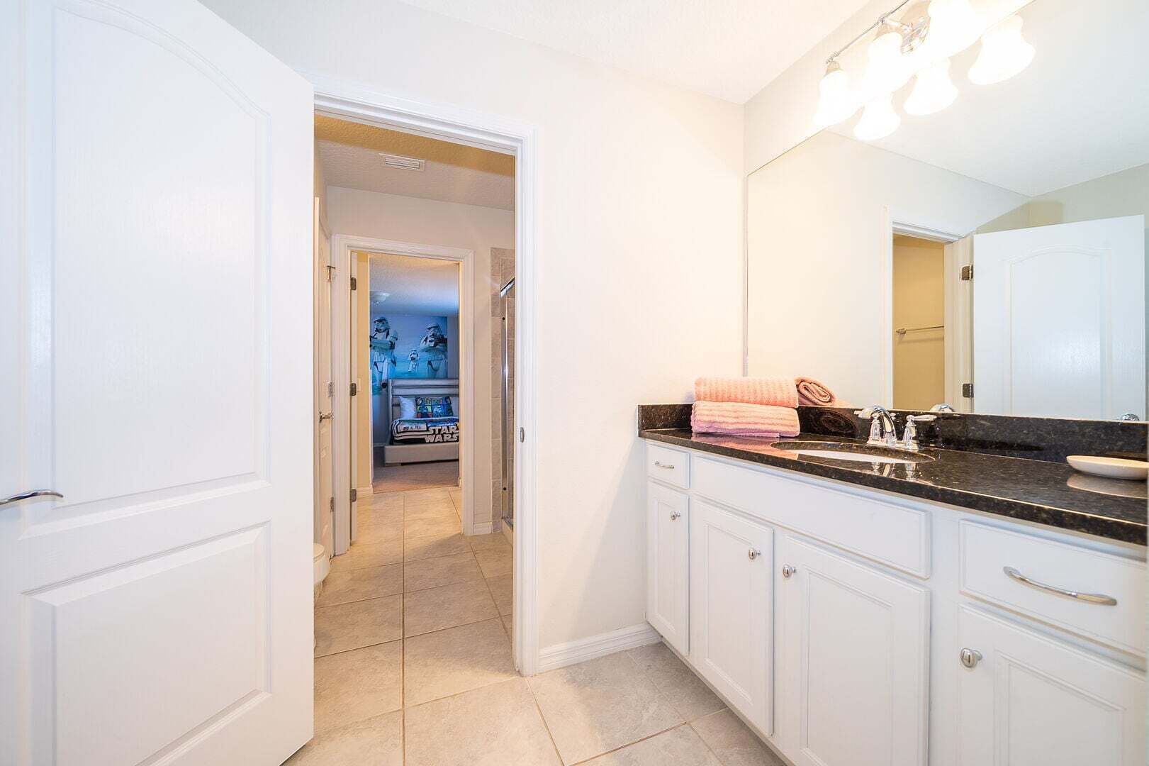 A bathroom with white cabinets, a black countertop, and a mirror.