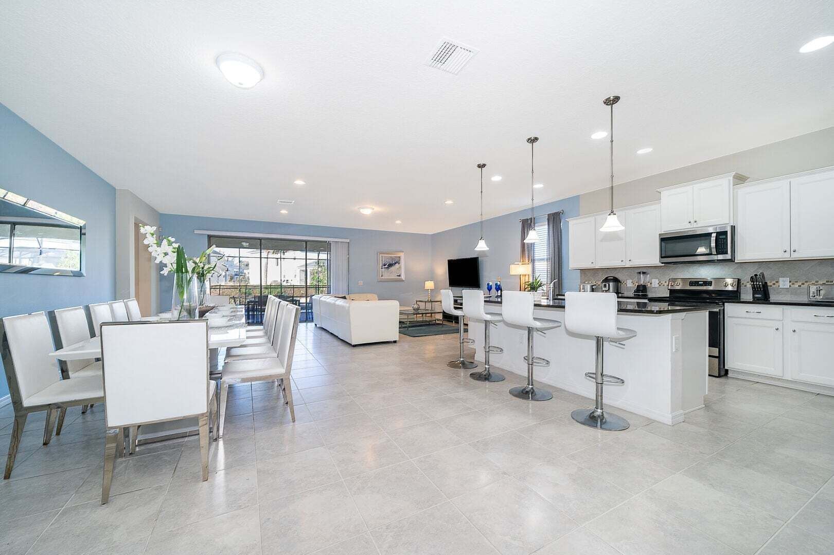 A modern kitchen with white cabinets, a central island, and a dining area with white chairs.