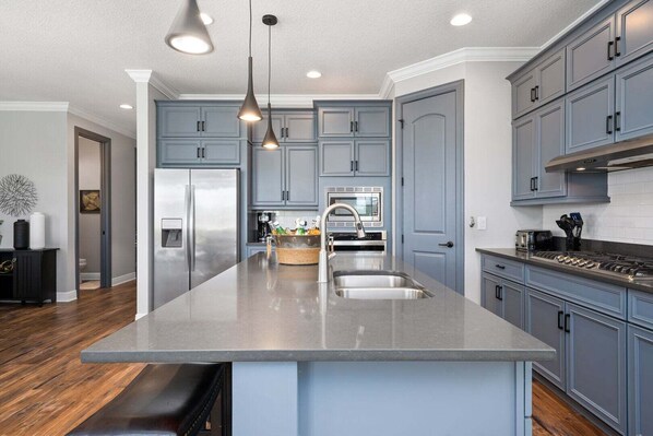 A modern kitchen with grey cabinets, stainless steel appliances, and pendant lighting. - Boutique Luxury Home, Private Pool Close to Disney (Kissimmee)