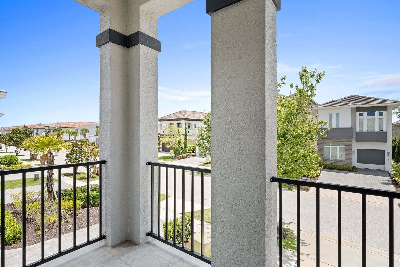 A balcony with a view of a residential area, featuring a modern house with a garage and a well-maintained lawn.