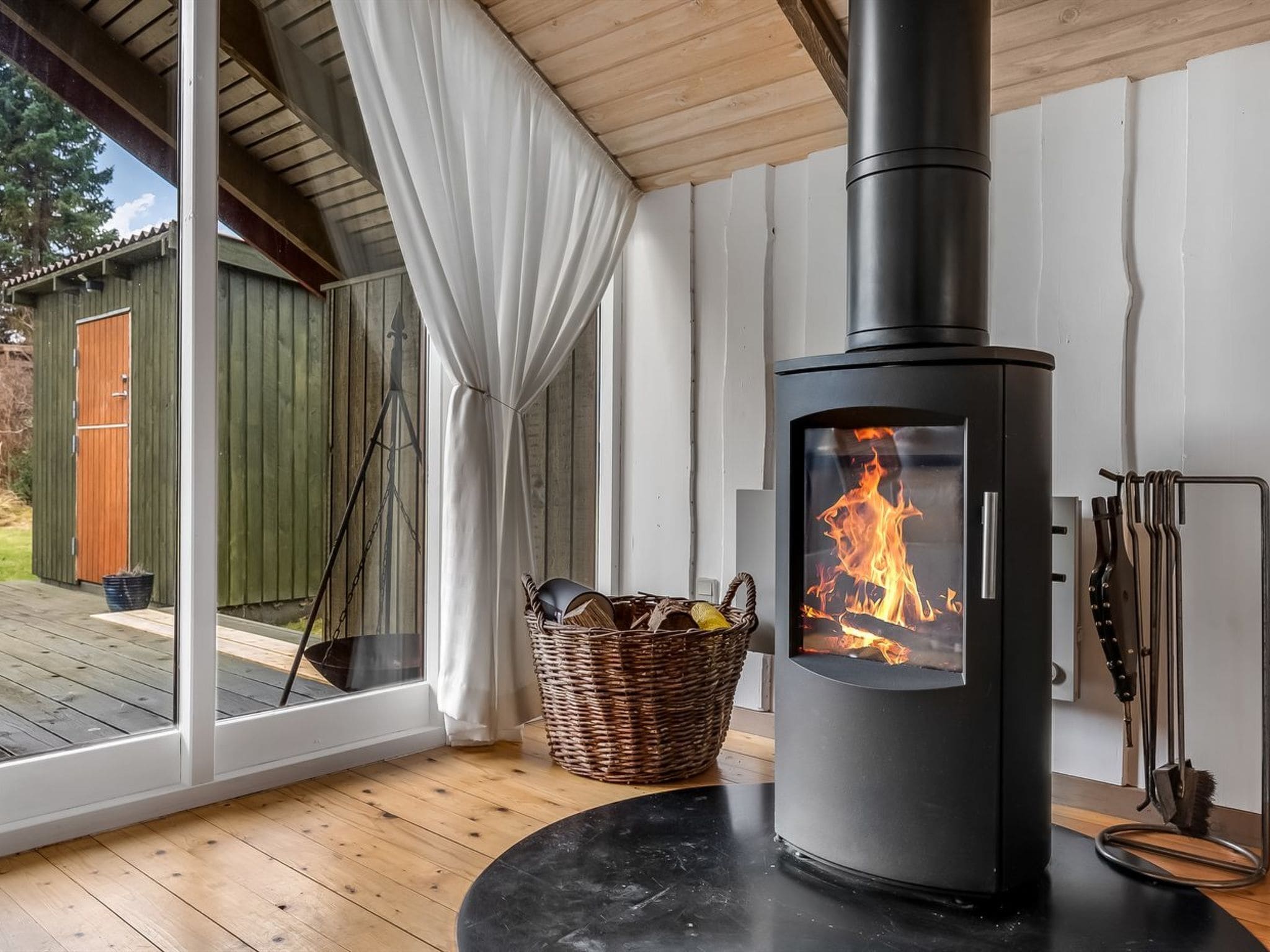 A modern interior with a wood-burning stove, a wicker basket, and a view through a glass door.