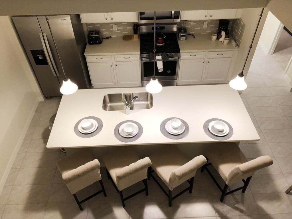 A modern kitchen with a central island, four chairs, a refrigerator, a stove, and a sink.
