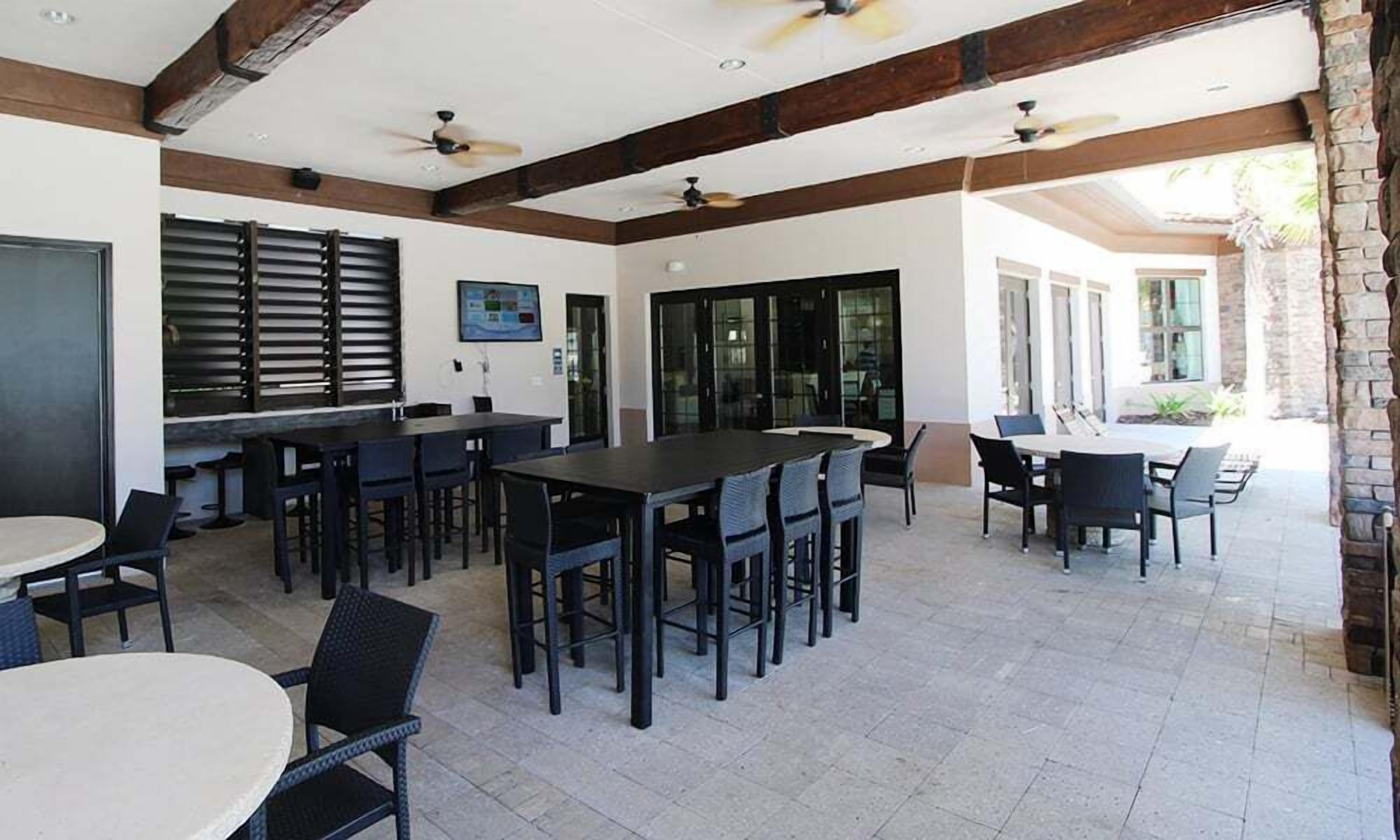 A spacious outdoor dining area with multiple tables and chairs, ceiling fans, and large windows.