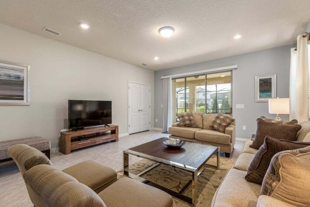A living room with a television, sofa, coffee table, and a sliding glass door to the outside.