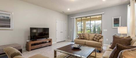 A living room with a television, sofa, coffee table, and a sliding glass door to the outside.