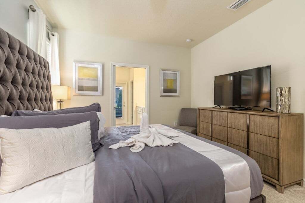 A hotel room with a large bed, a television, a wooden cabinet, and a door leading to a balcony.