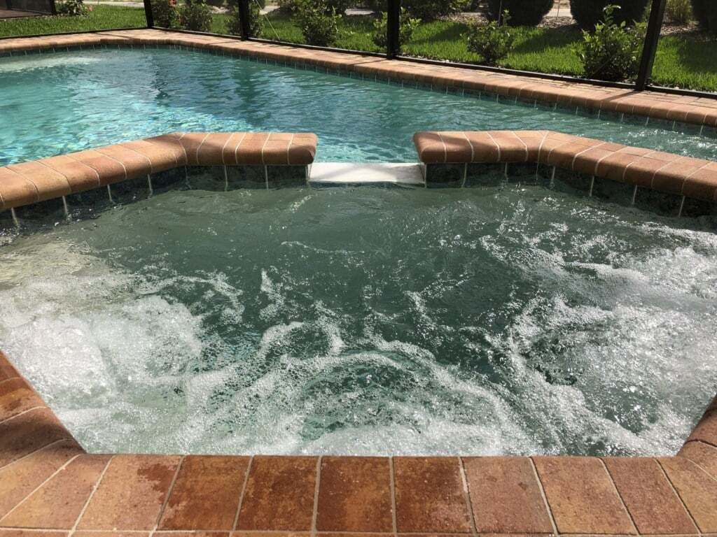 Una vasca idromassaggio con cascata, circondata da un bordo in mattoni e da un'area verde.
