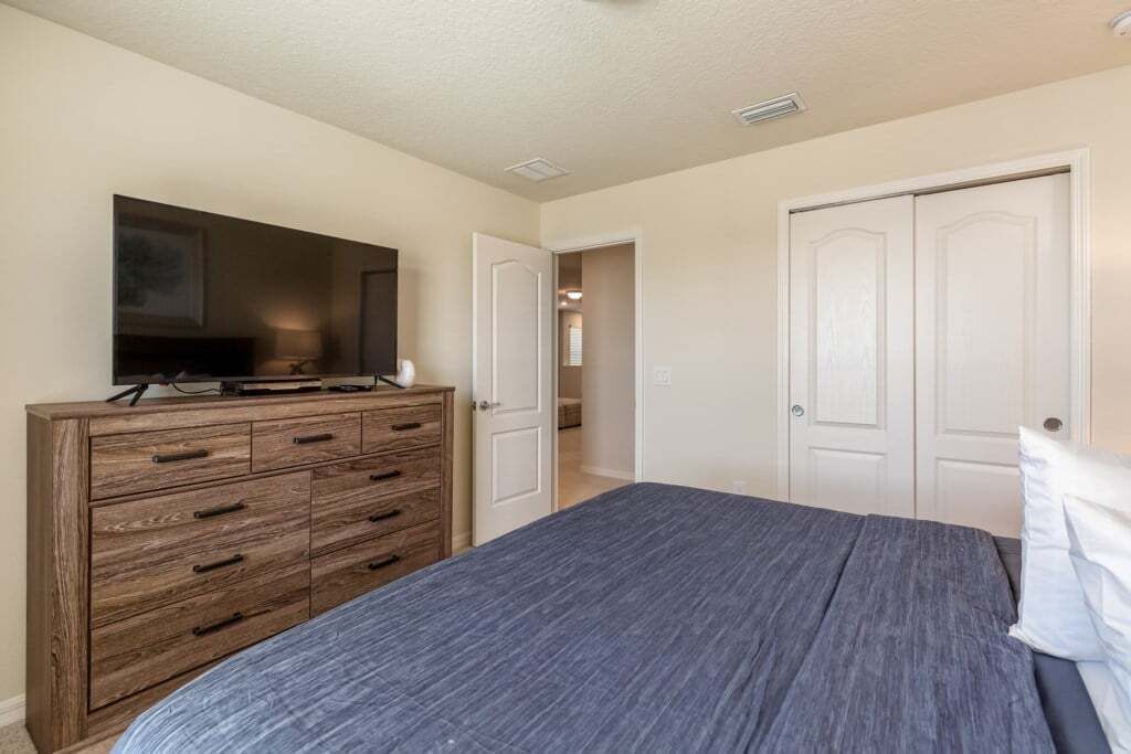 A bedroom with a bed, a dresser, a television, and two doors.