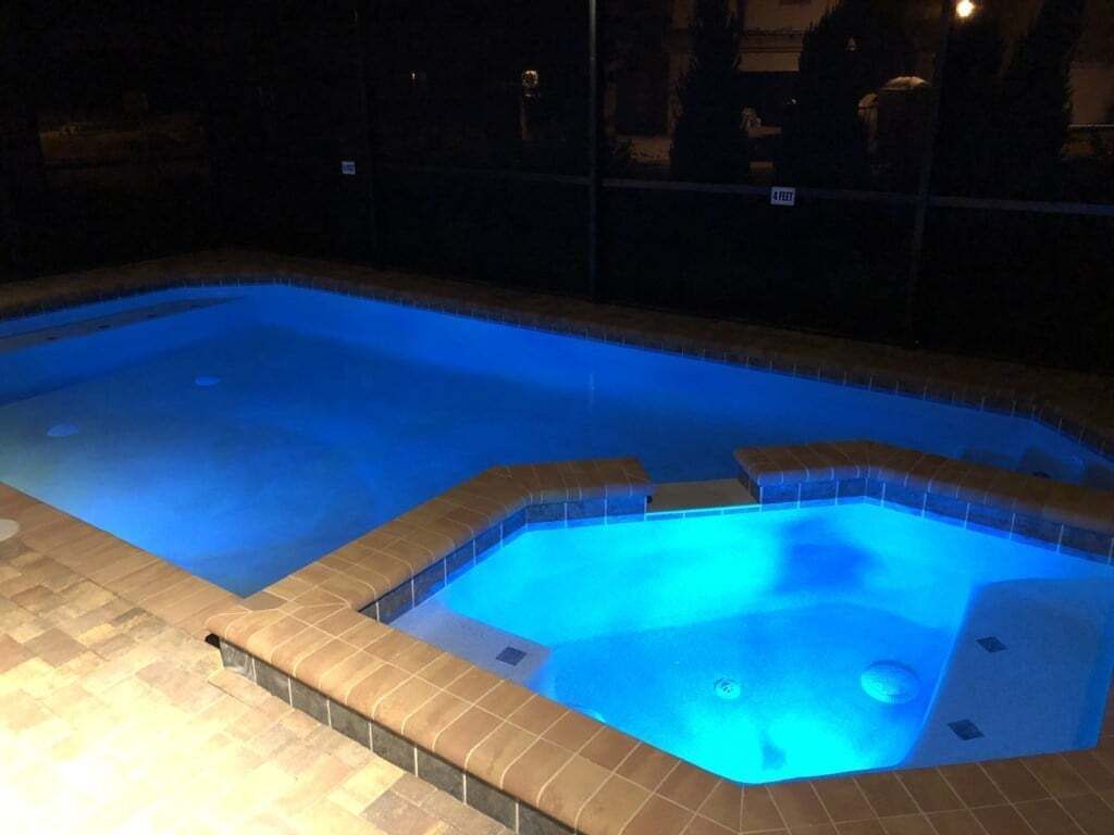 A swimming pool with a tiled edge and a hot tub area.