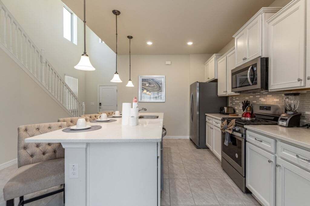 A kitchen with a central island, white cabinetry, stainless steel appliances, pendant lighting, and a staircase on the left.