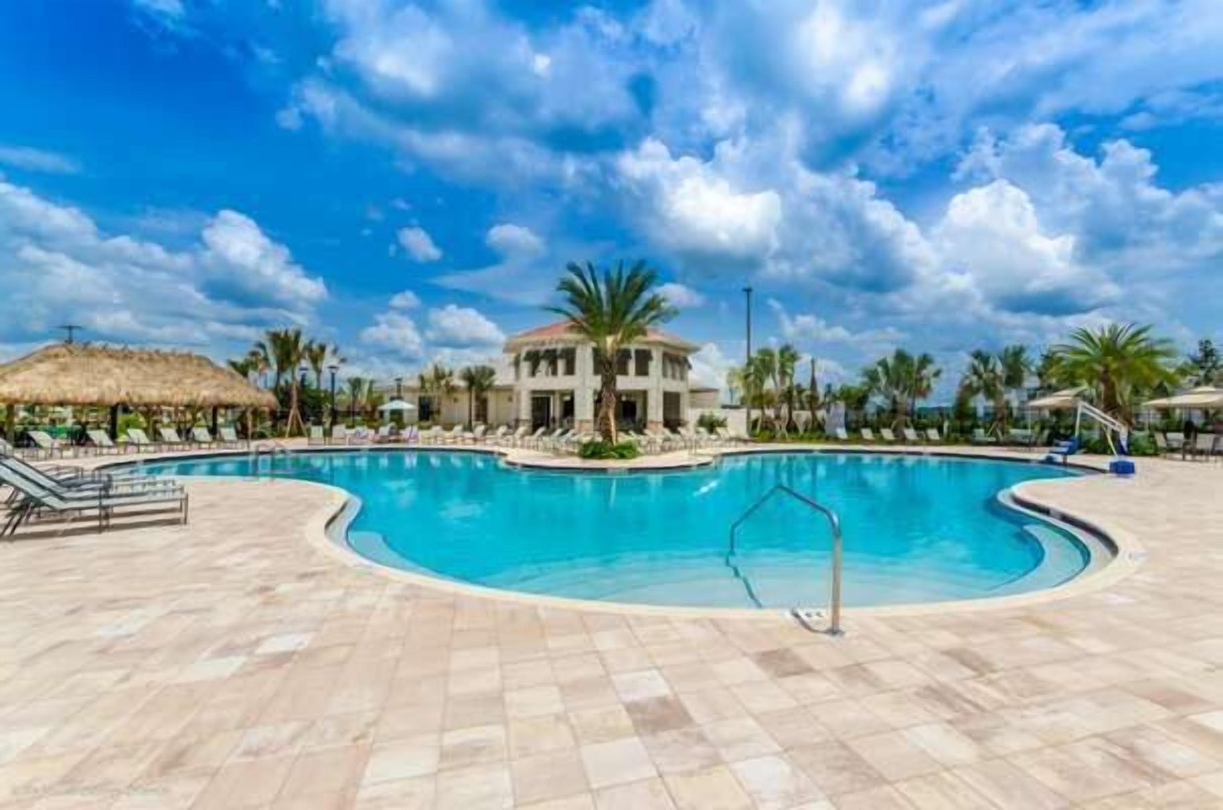 A swimming pool with lounge chairs, a building with a dome roof, palm trees, and a clear sky.