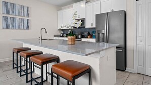 Una cucina moderna con pensili e basi bianche, un frigorifero in acciaio inox, una grande isola con sgabelli e un piano di lavoro rivestito di piastrelle blu.