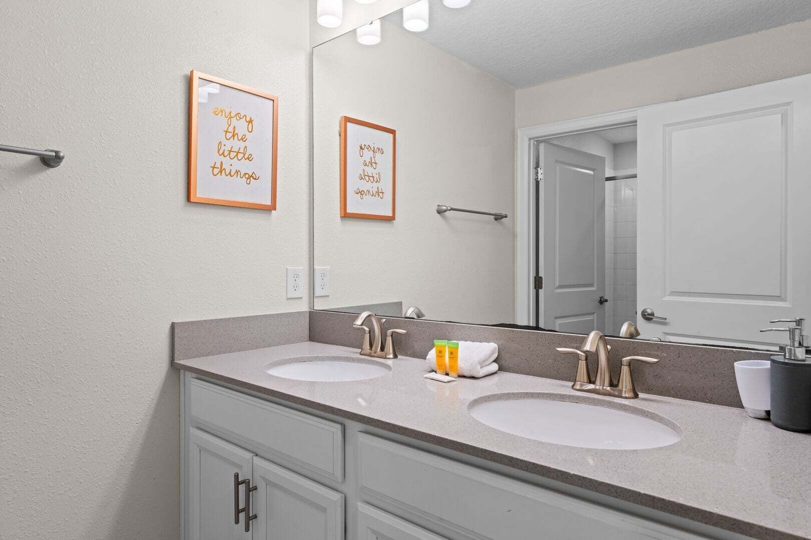 A bathroom with two sinks, a mirror, and framed inspirational quotes.