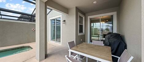 A covered patio with a pool, a table with chairs, and a grill.