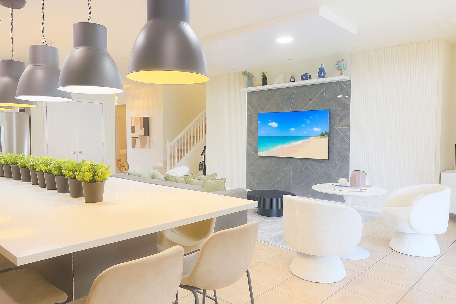 A modern kitchen with a long island, pendant lighting, and a large TV on the wall.
