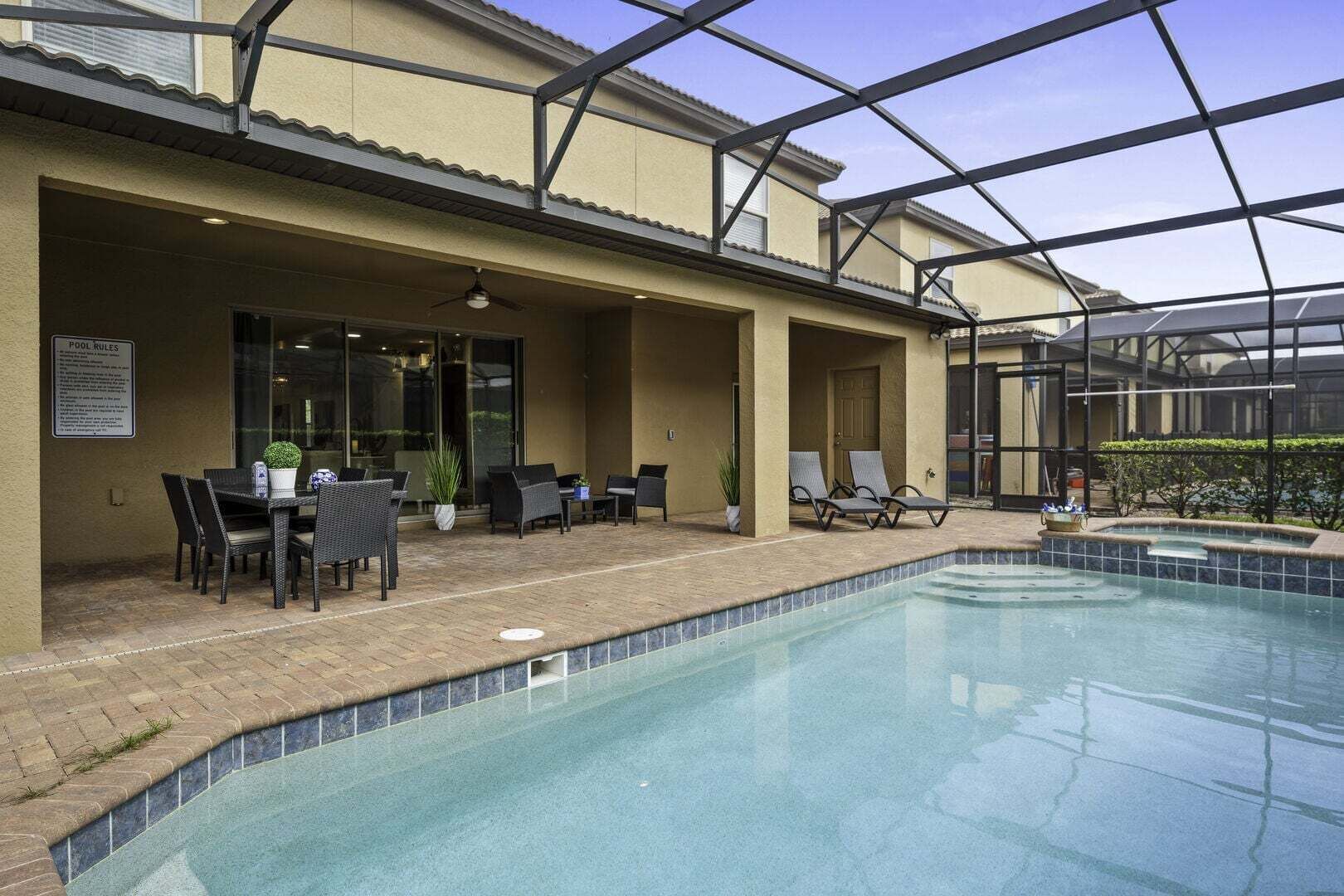A covered outdoor pool area with lounge chairs, a table, and a signboard.