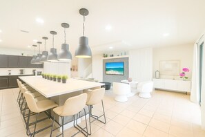 A modern kitchen with a central island, bar stools, pendant lighting, and a large TV on the wall. - Comfortable Vacation Home - Great Resort Pool/spa Sleeps 20 Ww101 (Kissimmee)