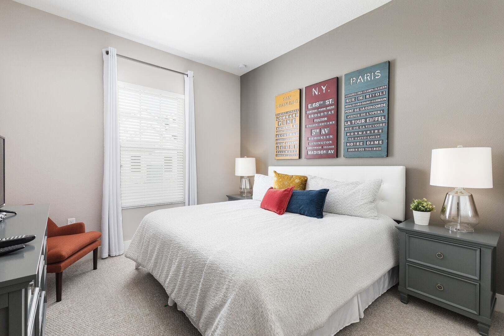 A hotel room with a bed, bedside tables, a desk, and a window with blinds.