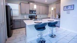 A modern kitchen with grey cabinets, a black refrigerator, a microwave, and a central island with bar stools. - Champions Gate Gem Pool, Spa, Near Parks (Davenport)