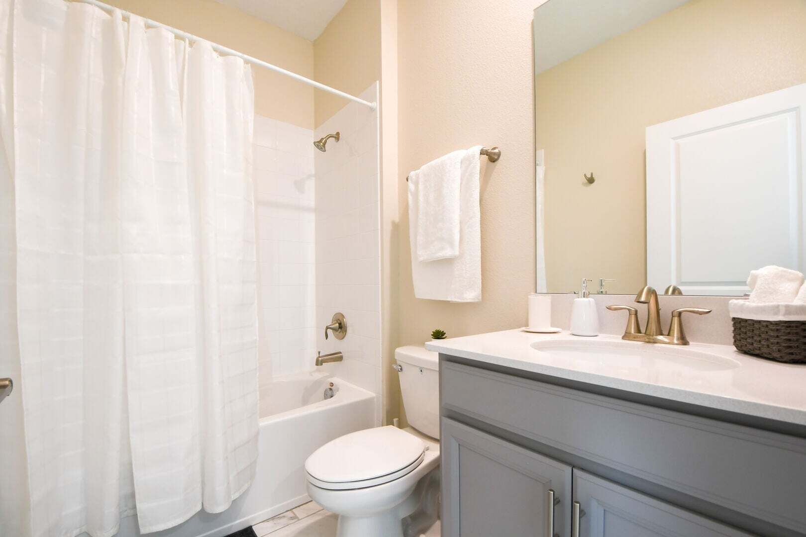 A bathroom with a shower, toilet, sink, and mirror.