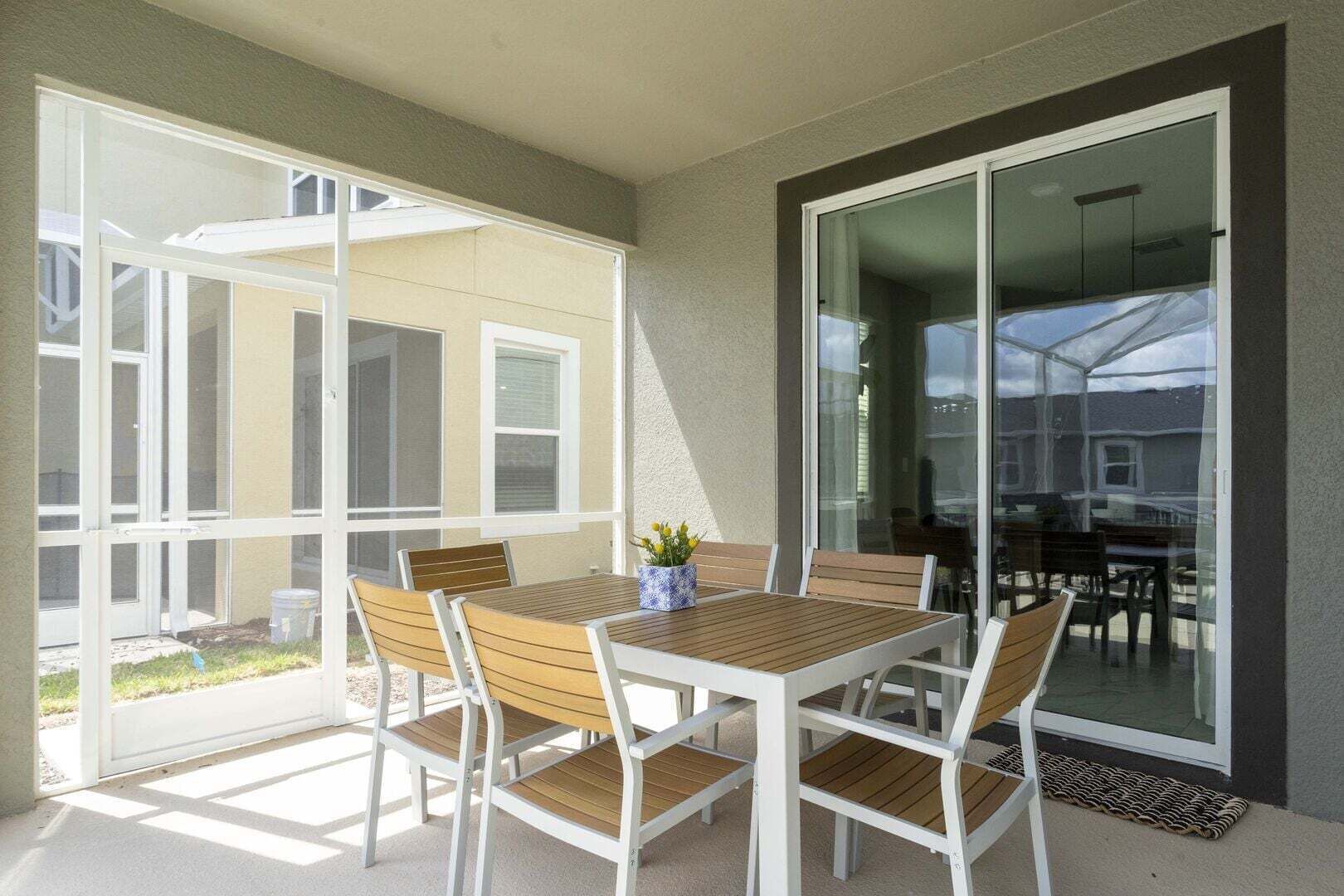 A patio with a table and chairs, a glass door, and a view of a house.
