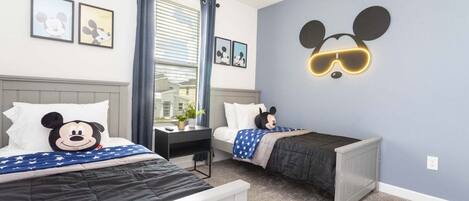 A hotel room with two beds, a Mickey Mouse wall decoration, and framed pictures on the wall.