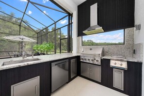 Eine moderne Küche mit großem Fenster, integriertem Grill und Blick ins Freie.