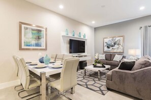 A modern living room with a dining area, a flat-screen TV, and artwork on the walls. - Precious Townhome BBQ 131 (Kissimmee)
