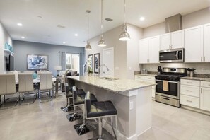 A modern kitchen with white cabinets, stainless steel appliances, and a central island with bar stools. - Precious Townhome BBQ 131 (Kissimmee)