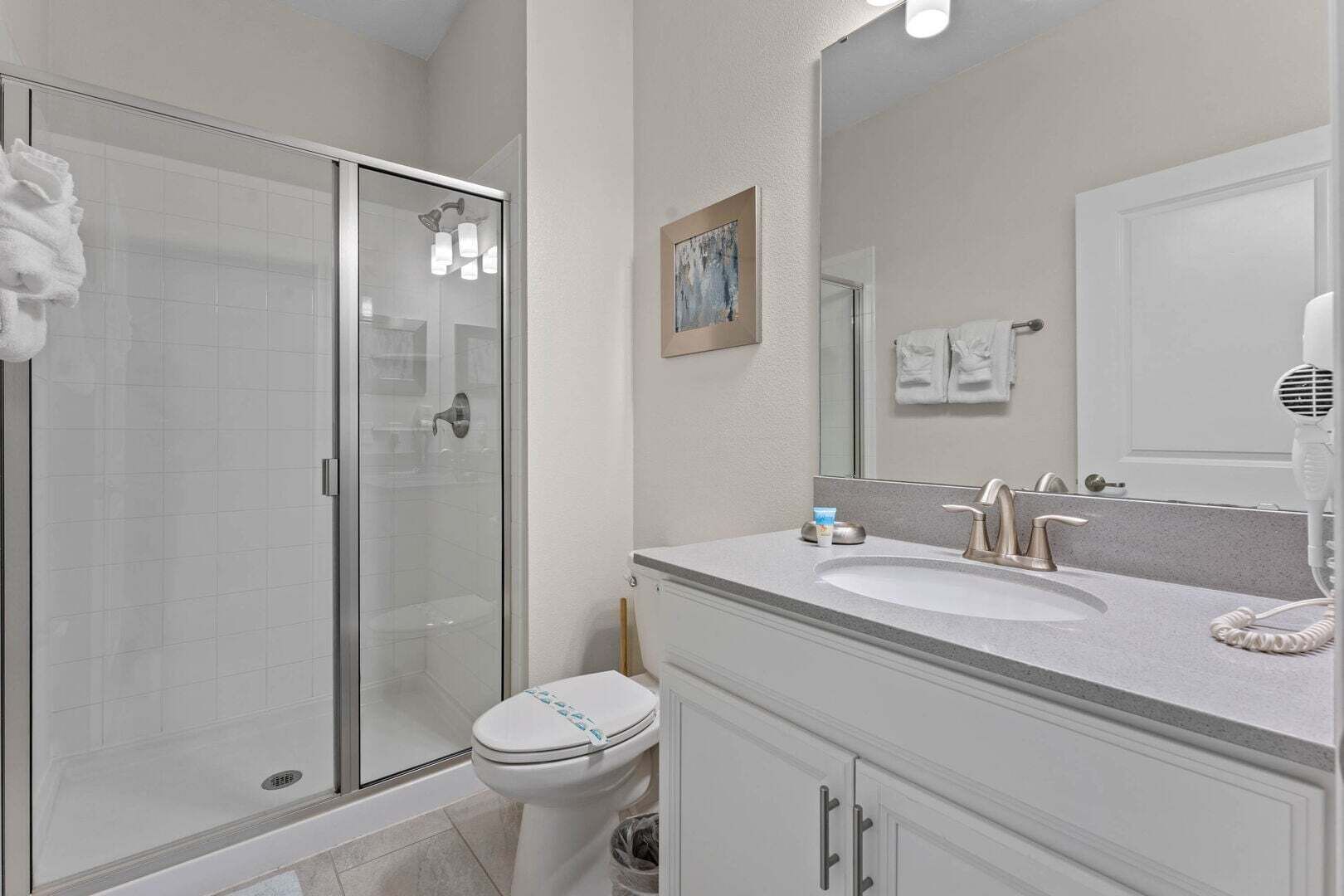 Un baño con cabina de ducha de vidrio, inodoro, lavabo con tocador y secador de pelo.