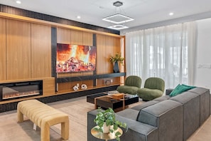 Ein modernes Wohnzimmer mit großem Flachbildfernseher, einer Couch, zwei Sesseln, einem Couchtisch und einem Kamin.