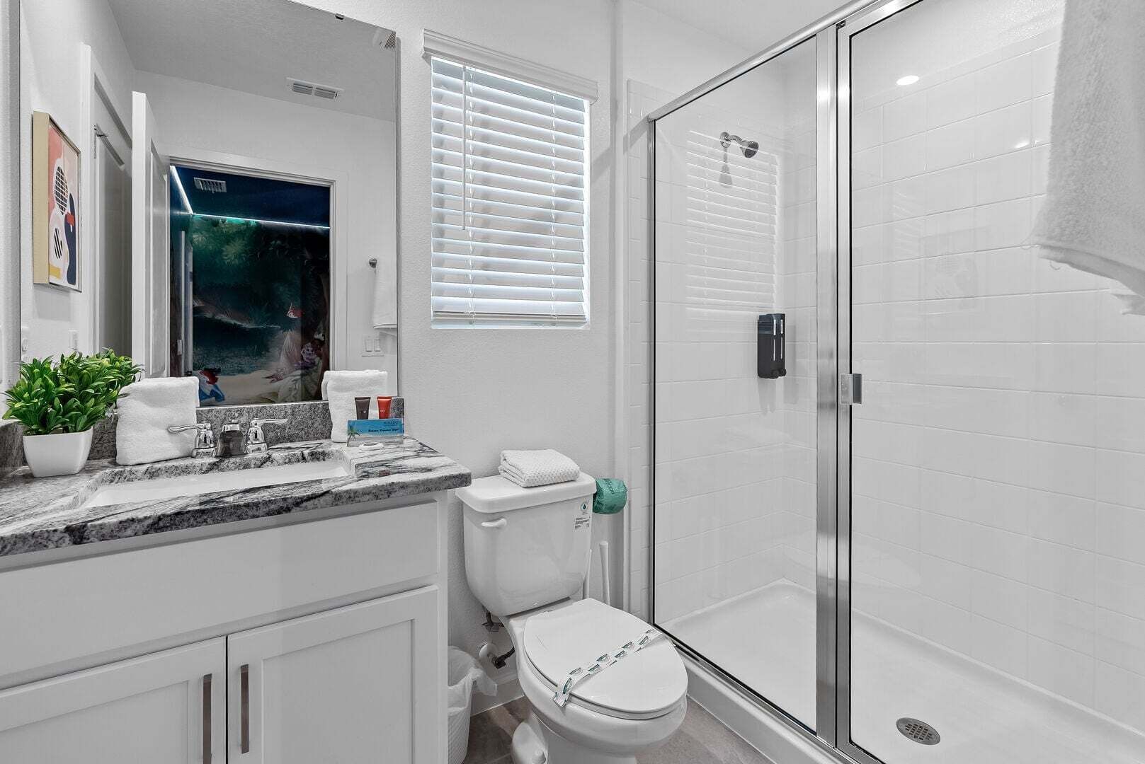 A modern bathroom with a glass shower enclosure, a white toilet, a marble sink, and a potted plant.