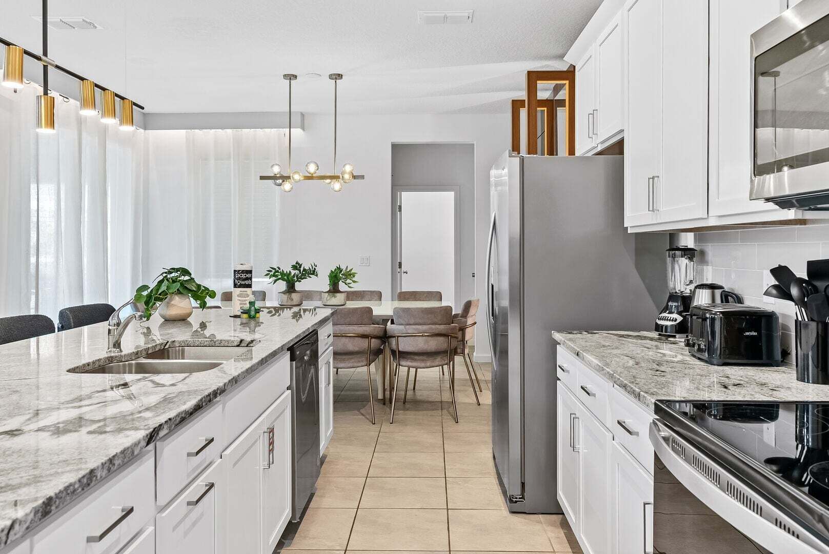 A modern kitchen with a marble countertop, stainless steel appliances, and a dining area with a chandelier.