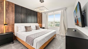 Un dormitorio moderno con una cama grande, cabecera de madera, mesita de noche, escritorio y ventana con cortinas.