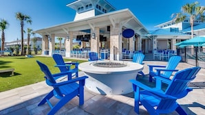 Un espace extérieur aménagé, abrité et doté de chaises Adirondack bleues, d’un foyer central et d’un bar au bord de la piscine.