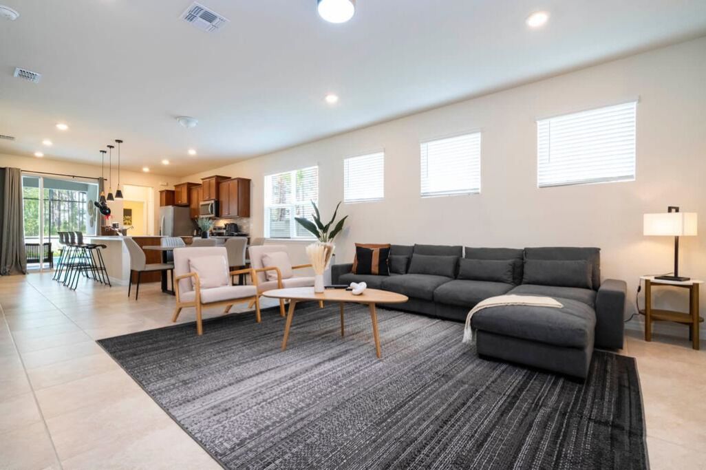 A modern living room with a grey sofa, a coffee table, and a dining area with chairs and a table.