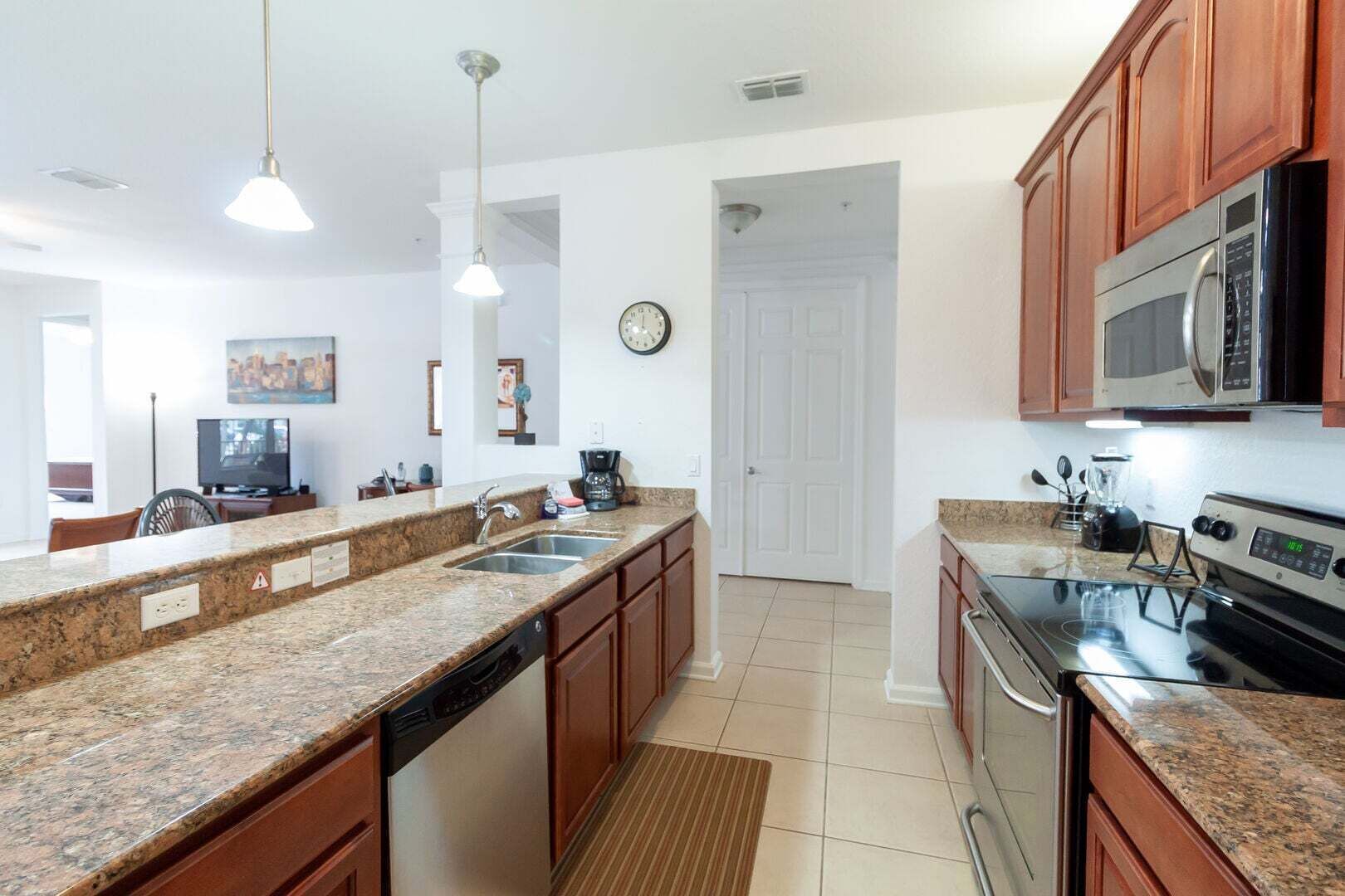 A kitchen with granite countertops, stainless steel appliances, wooden cabinets, a dishwasher, and pendant lighting.