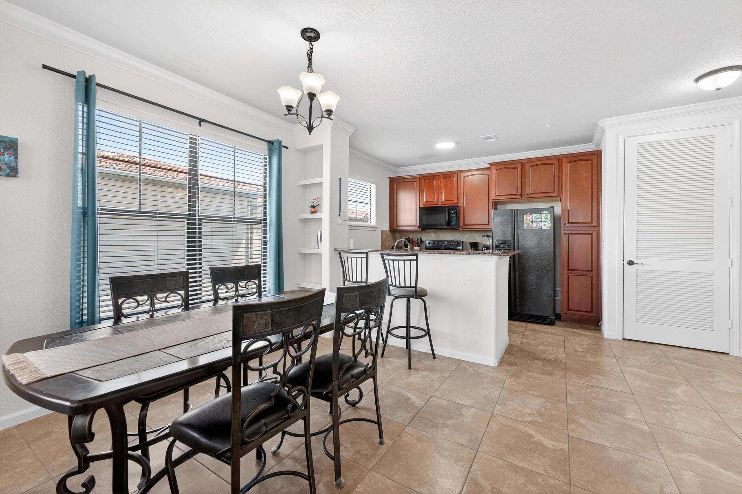 A modern kitchen with a dining area, featuring a central island, wooden cabinets, and a built-in microwave.