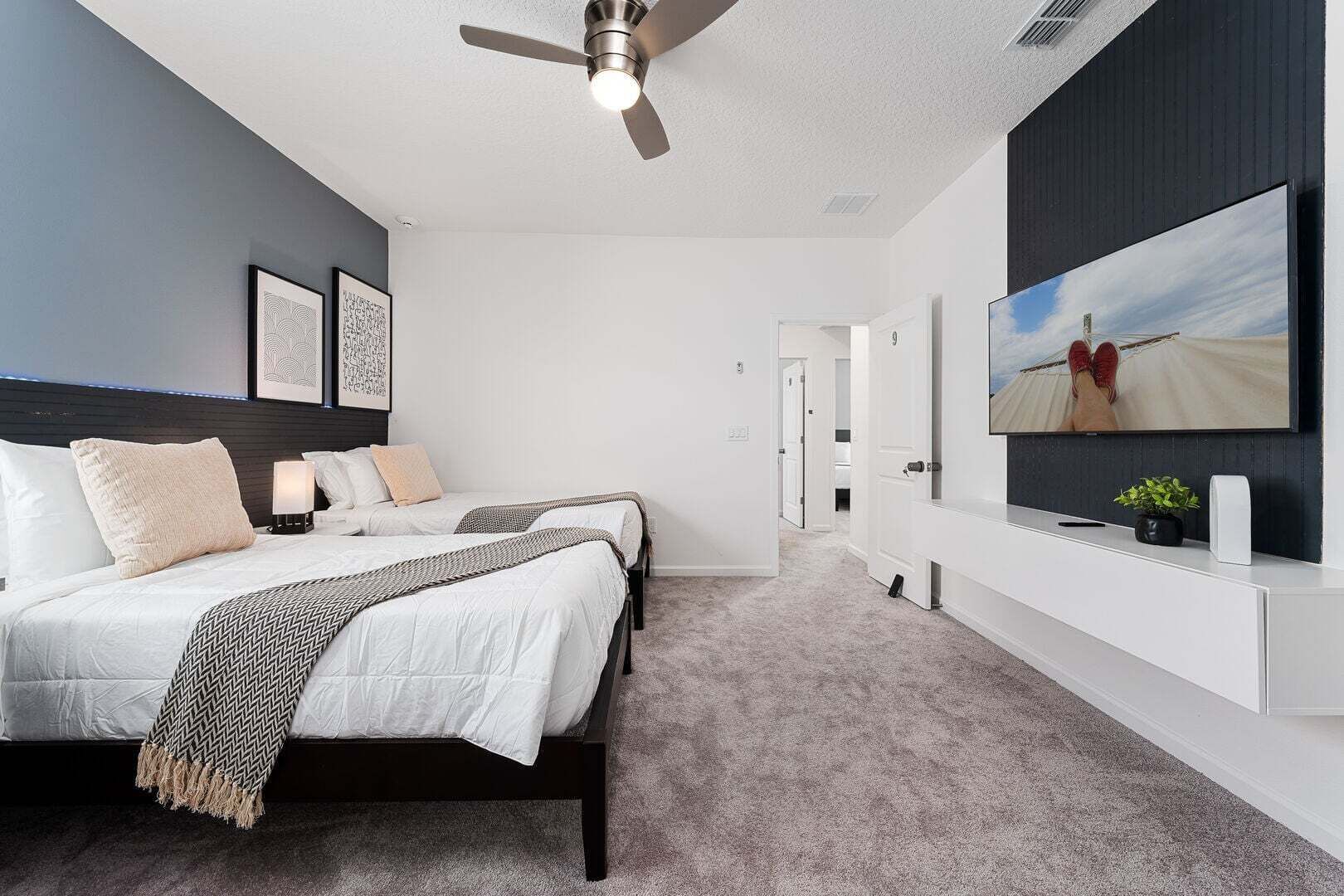 Een moderne slaapkamer met een bed, nachtkastjes, een plafondventilator, een televisie en een aan de muur bevestigde televisie.