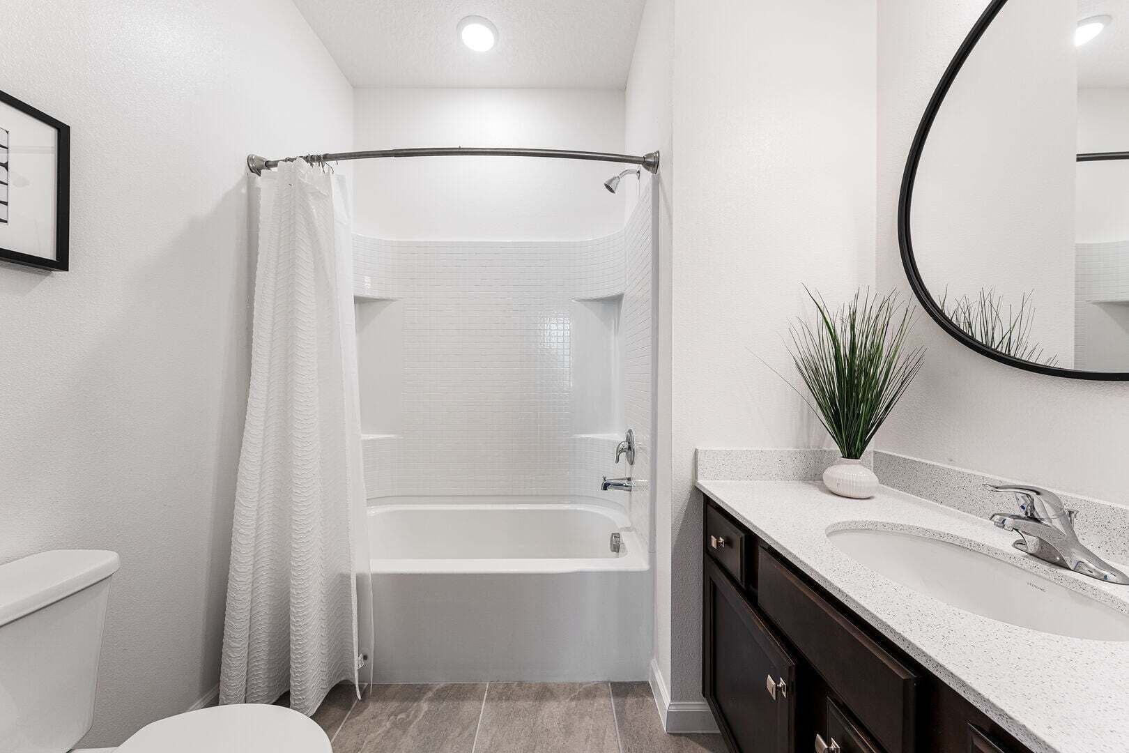 A modern bathroom with a bathtub, a toilet, a sink with a mirror, and a potted plant.