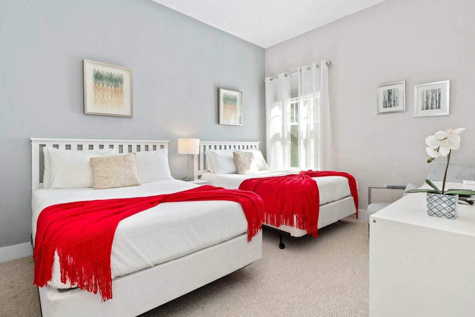 A hotel room with two beds, a desk, and a window with curtains.