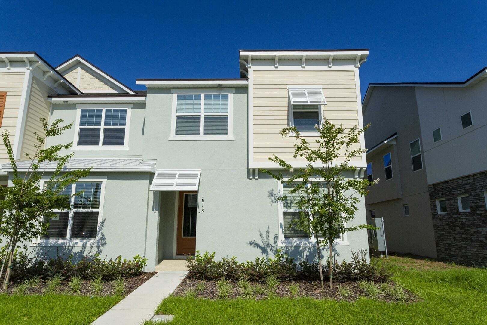 A modern multi-story residential building with a central entrance, a small porch, and a well-maintained lawn.