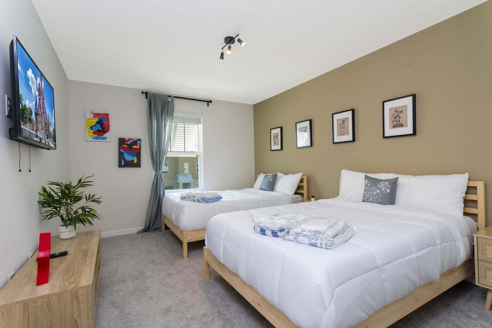 A hotel room with two beds, a TV, a plant, and artwork on the walls.