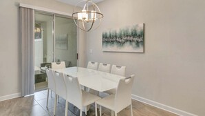 A dining area with a white table and chairs, a chandelier, and a painting on the wall. - Private Pool! 8 Min to Disney! (Kissimmee)