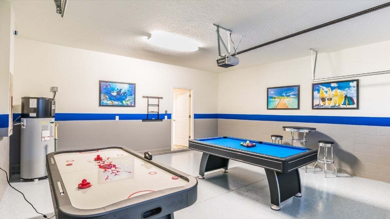 A pool table with a blue felt surface, a foosball table, and a projector mounted on the ceiling.