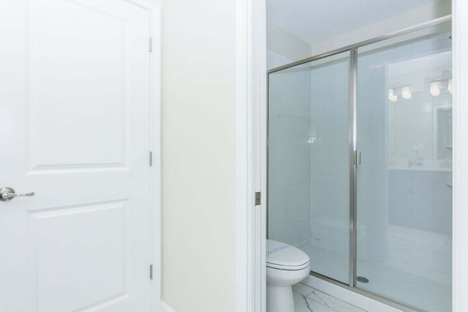 A bathroom with a white toilet, a glass shower enclosure, and a white door.
