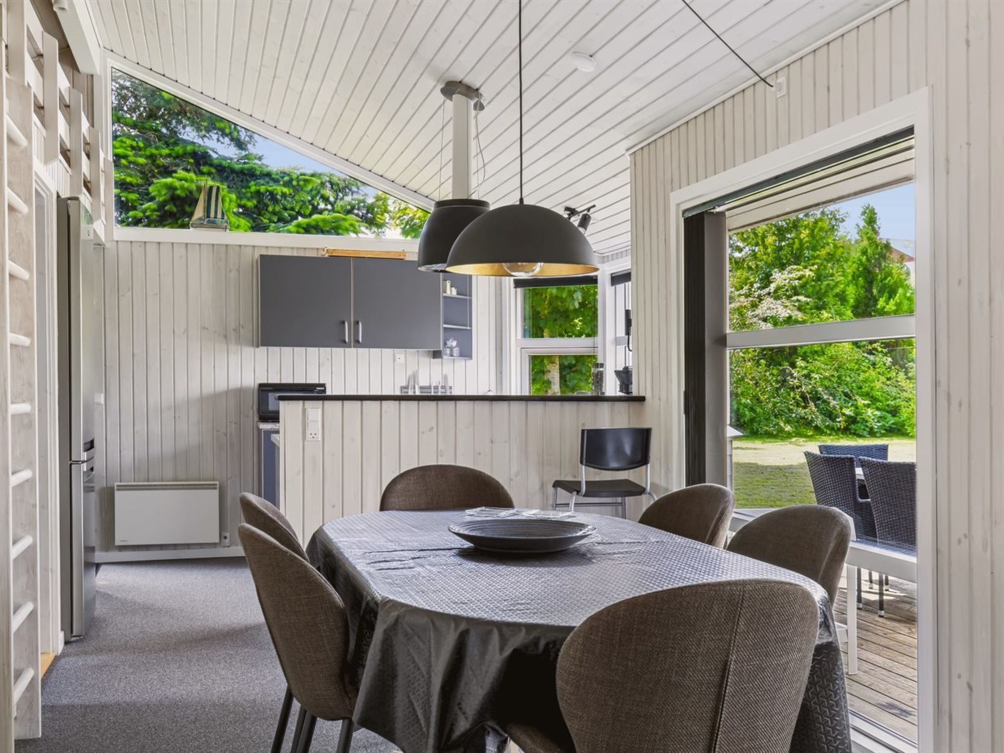 A modern kitchen with white cabinetry, a dining area with a table and chairs, and a large window overlooking greenery.