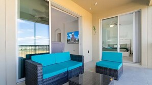 A balcony with a sofa and a coffee table, a sliding glass door, and a TV in the background. - Modern Stay w Full Resort-access Near Disney (Davenport)