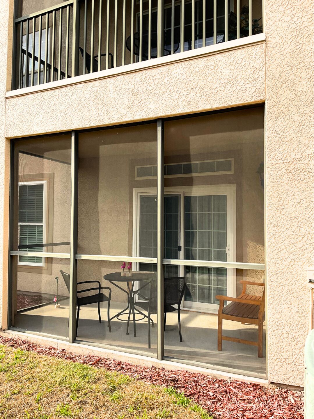 A modern building with large glass windows, a balcony with chairs, and a door with a window.